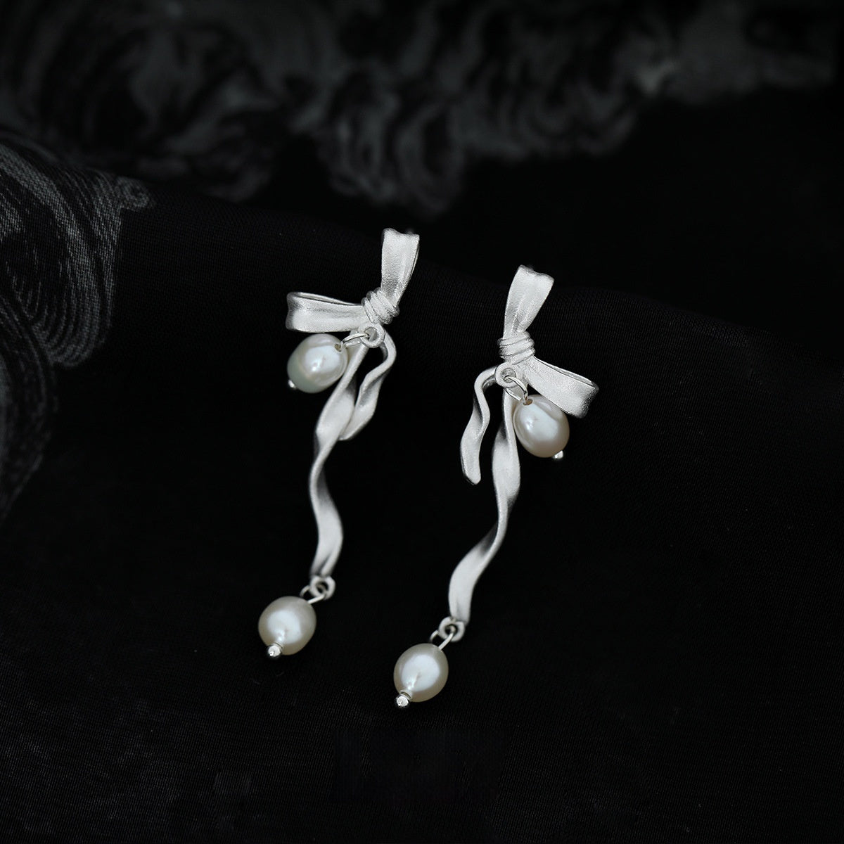 Bow-shaped stud earrings adorned with delicate pearls